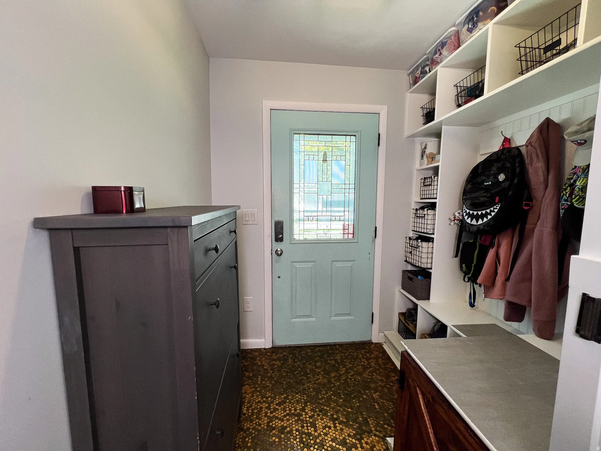 Entryway featuring a light blue door with decorative glass, built-in shelving, penny  flooring