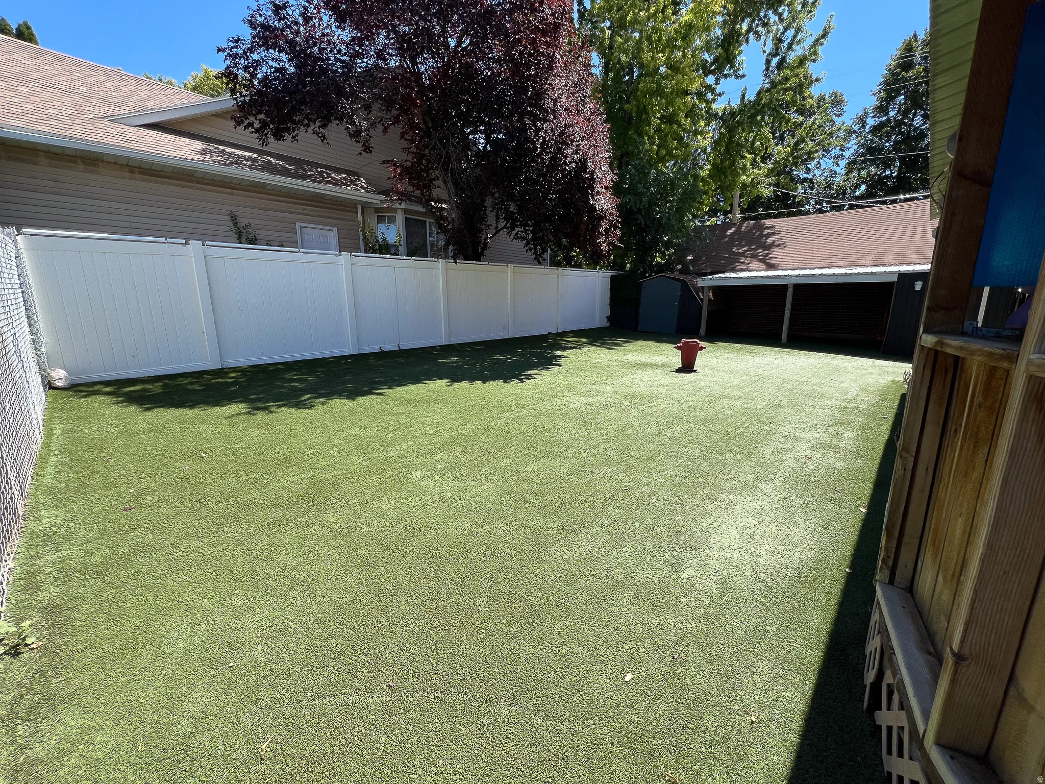 Expansive outdoor area featuring artificial turf, a white privacy fence, and a storage shed