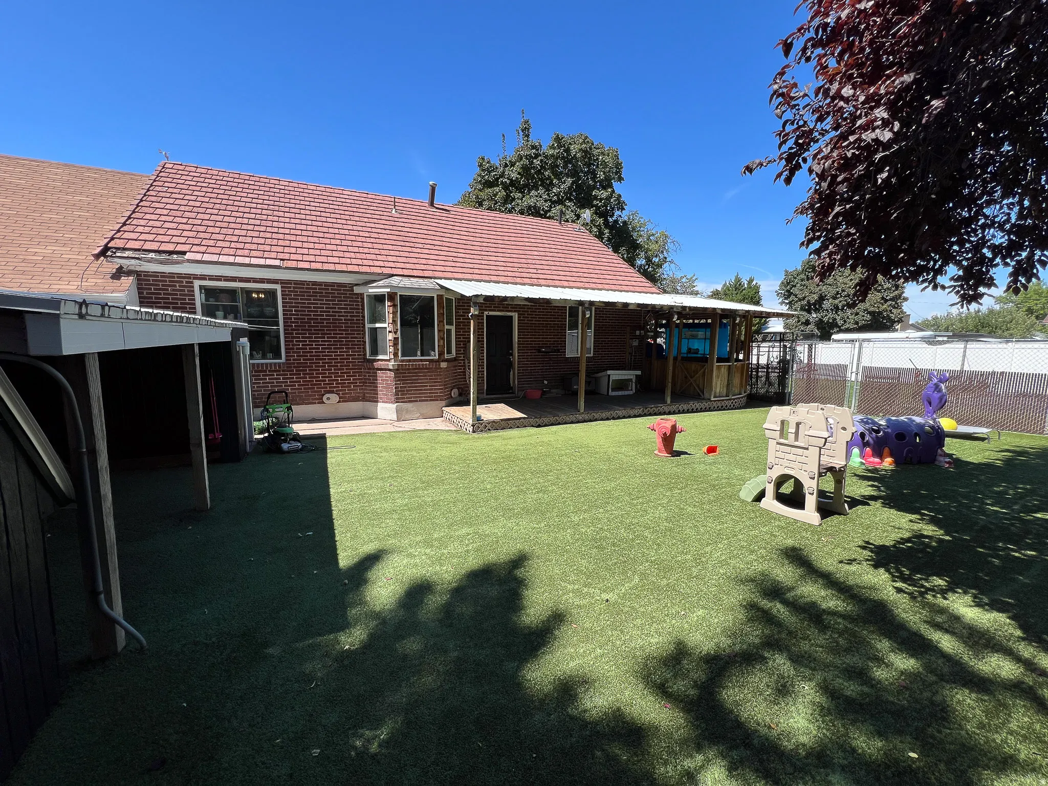 Brick exterior with a red tile roof, covered patio, artificial turf, and a detached garage