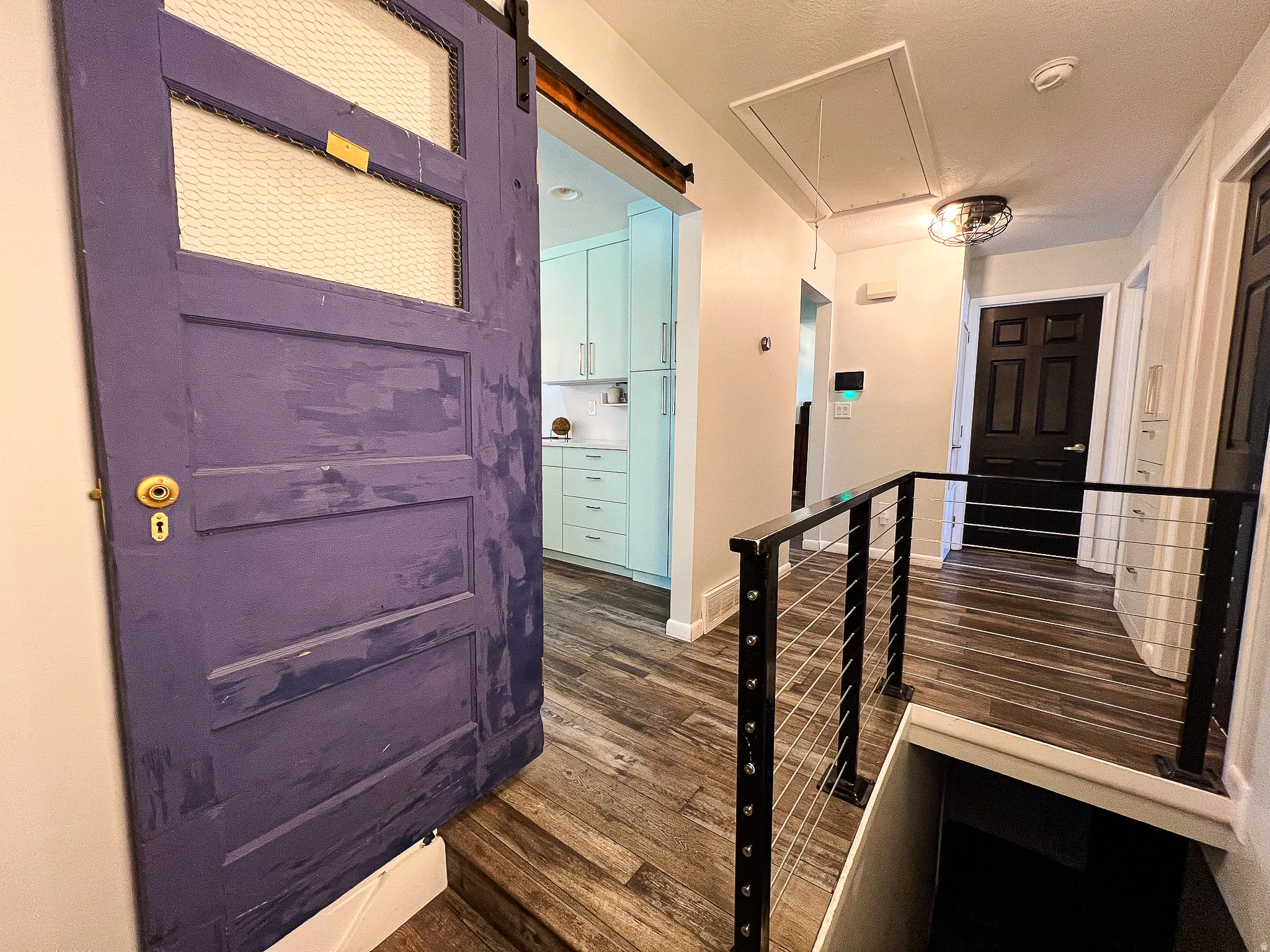 Sliding barn door, wood-finish flooring, black metal and cable railing, recessed lighting, and a contemporary ceiling fixture