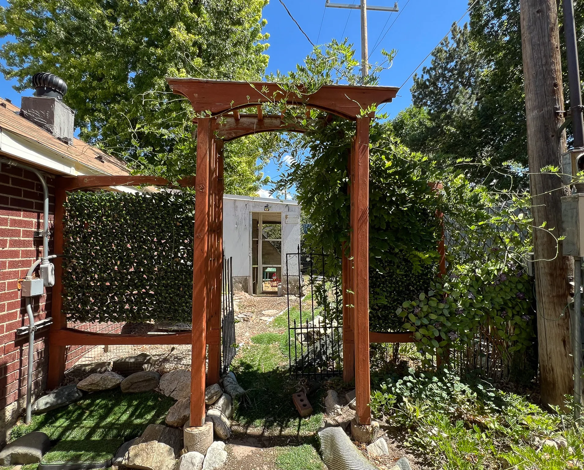 Wooden arbor entryway with established vines, brick exterior wall, and manicured green landscaping