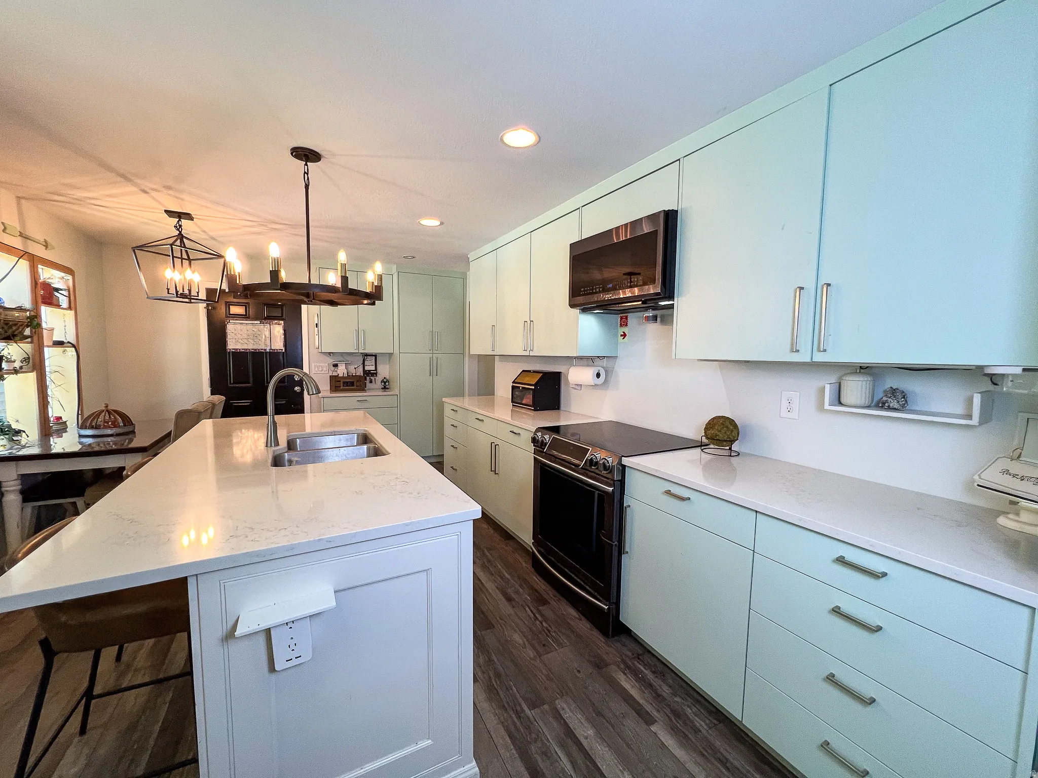 Kitchen featuring an island with an undermount sink, light-toned countertops, contemporary cabinetry, stainless steel appliances, and wood-finish flooring