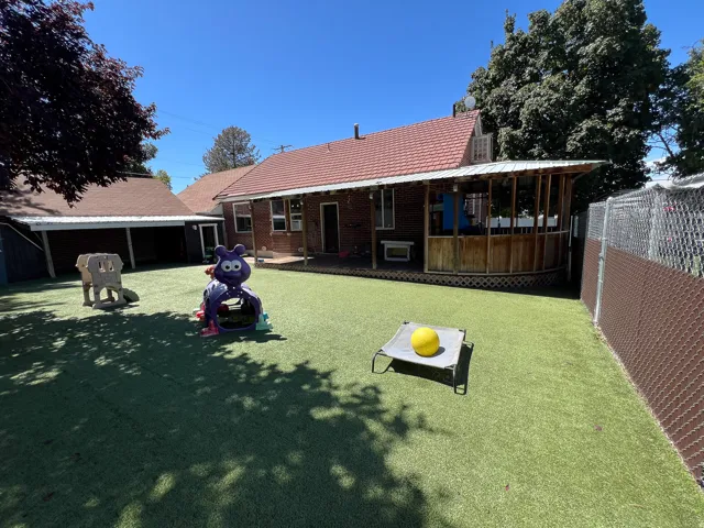 Expansive artificial turf backyard featuring a covered patio, brick exterior, and a chain link fence with privacy slats