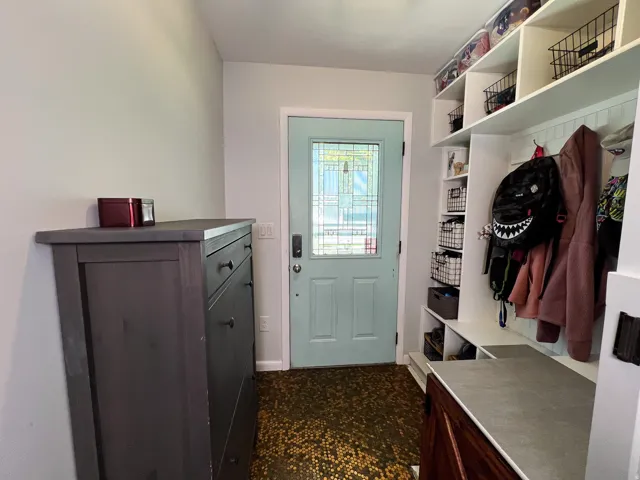 Entryway featuring a light blue door with decorative glass, built-in shelving, penny  flooring