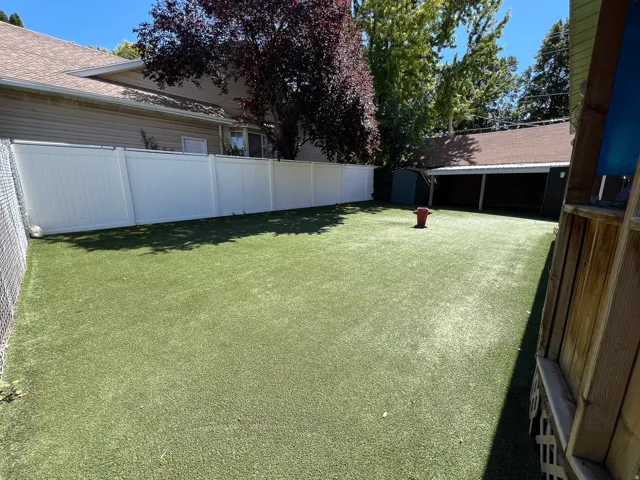 Expansive outdoor area featuring artificial turf, a white privacy fence, and a storage shed