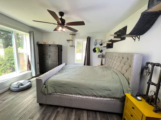 Room featuring wood-finish flooring, a ceiling fan with integrated lighting, and multiple windows