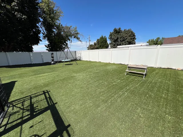 Expansive backyard featuring artificial turf and a white privacy fence