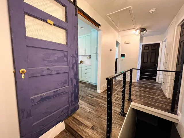 Sliding barn door, wood-finish flooring, black metal and cable railing, recessed lighting, and a contemporary ceiling fixture