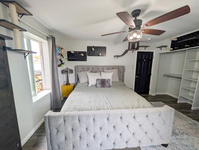 Wood-finish flooring, ceiling fan, built-in shelving, and a dark paneled door