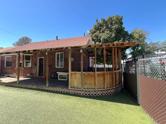 Brick exterior with a covered deck featuring a built-in privacy enclosure, synthetic turf backyard, and chain-link fencing