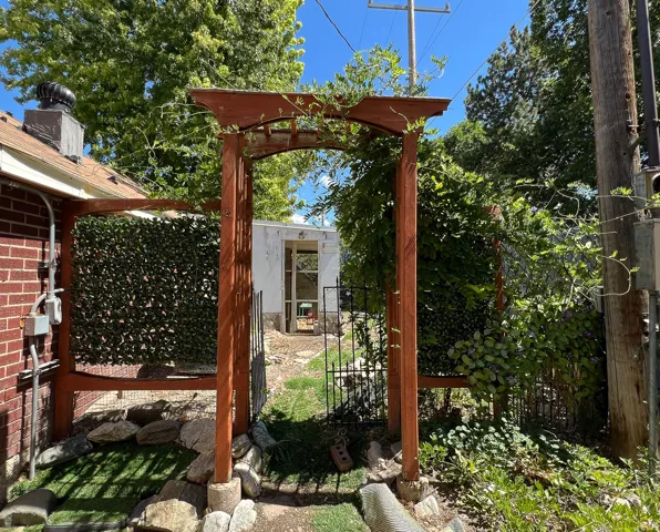 Wooden arbor entryway with established vines, brick exterior wall, and manicured green landscaping