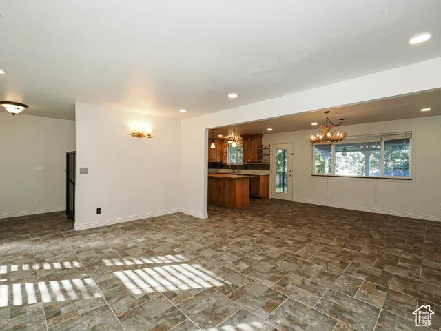 Open-concept interior featuring stone-finish tile flooring, recessed ceiling lighting, decorative antler-style chandeliers, and natural wood cabinetry