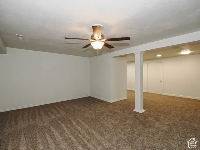 Spacious room featuring neutral carpeting, a central ceiling fan with integrated lighting, recessed ceiling lights, and a structural support column