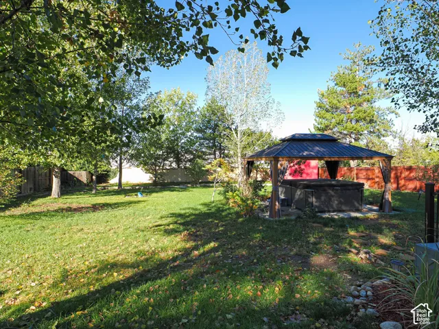 Spacious backyard featuring a manicured lawn, mature trees, a permanent metal-roof gazebo, and a built-in spa
