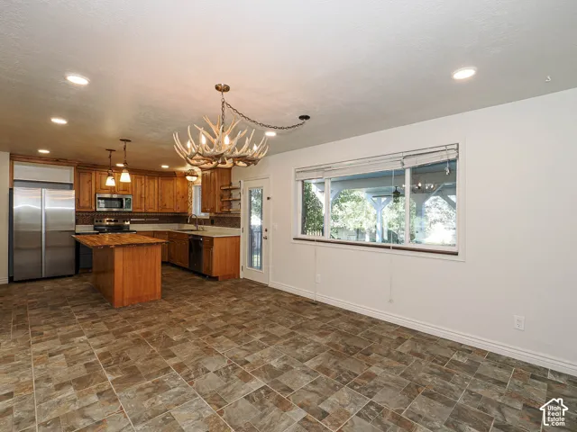 Kitchen featuring natural wood cabinetry, stainless steel appliances, a center island with a wood countertop, stone-pattern tile flooring, and decorative antler chandelier