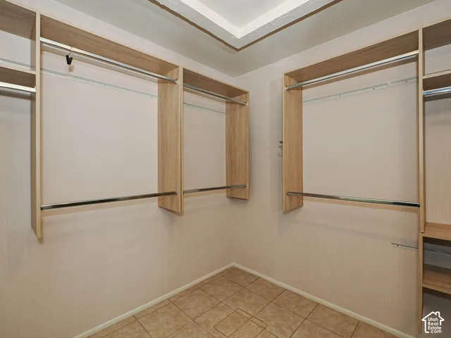 Walk-in closet featuring light-toned wood-finish built-in shelving, chrome hanging rods, recessed ceiling lighting, and ceramic tile flooring