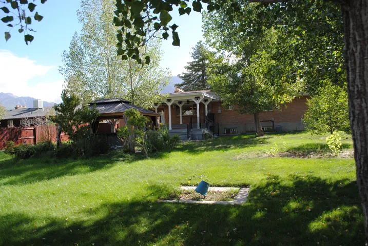 Expansive green lawn featuring mature trees, a covered gazebo, and a brick exterior residence with a decorative porch