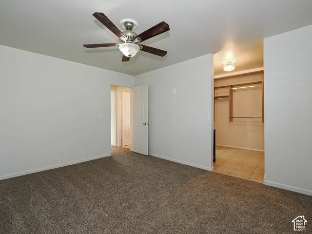 Interior space featuring neutral-toned carpeting, a ceiling-mounted fan with integrated lighting, a walk-in closet with built-in shelving, and tile flooring