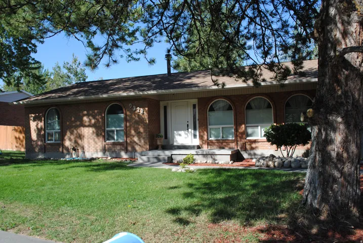 Brick facade with arched window accents, white entry door, concrete front steps, and mature front yard landscaping