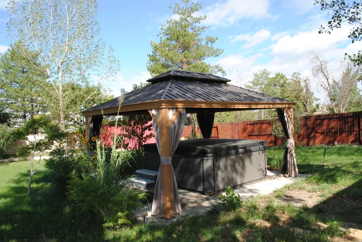 Private backyard oasis featuring a hot tub within a gazebo, surrounding greenery, and a solid perimeter fence