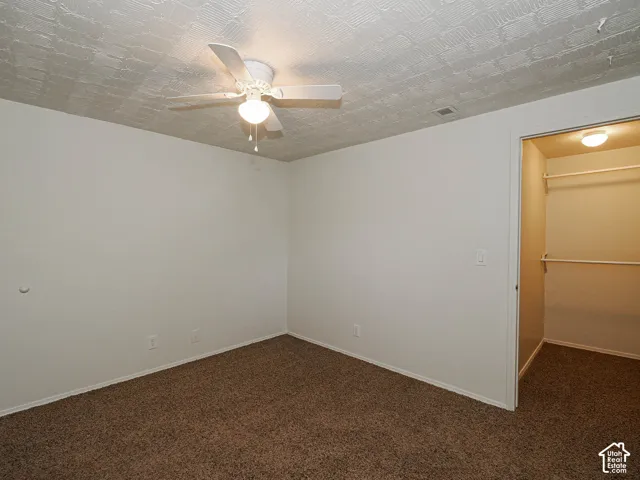 Neutral-toned room featuring textured ceiling finish, ceiling-mounted light fixture with fan, and closet with built-in shelving