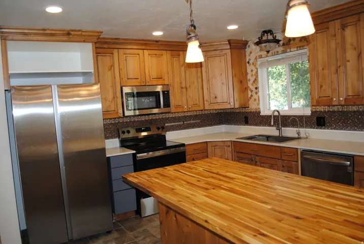 Kitchen featuring wood cabinetry, stainless steel appliances, a wood-finish island countertop, light-toned perimeter countertops, and a patterned tile backsplash