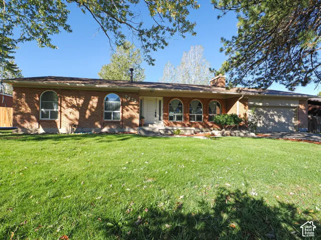 Single-story brick exterior featuring arched windows, a masonry chimney, an attached garage, and mature landscaping