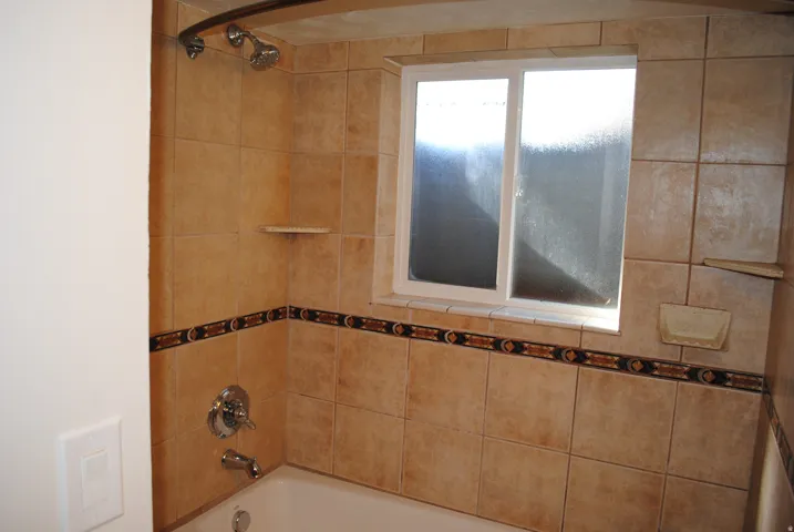 Bathtub with ceramic tile surround, decorative tile accent band, and integrated shower head