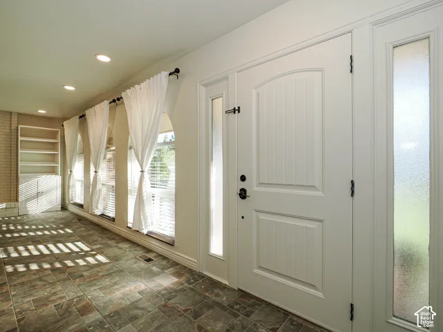 Entryway featuring multi-toned tile flooring, recessed lighting, arched windows with blinds, a  storage cabinet, and a white front door with dual frosted sidelights