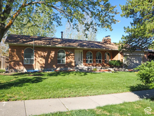 Single-story brick exterior featuring an arched window design, shingled roof, exterior brick chimney, and attached garage