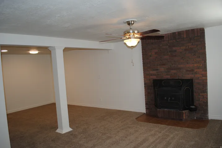 Brick fireplace with hearth, ceiling fan with integrated lighting, recessed lighting, carpeted flooring, and structural columns