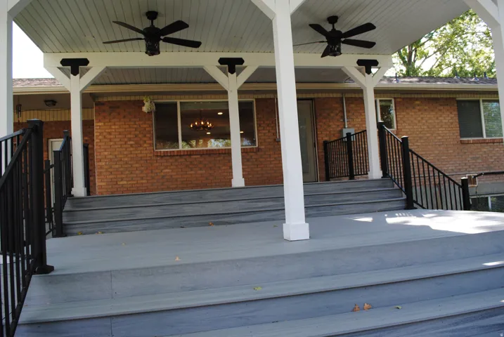 Covered outdoor deck with white support columns, gray composite decking, and black metal railings
