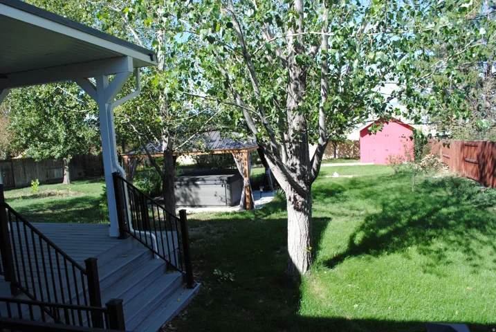 Expansive backyard featuring a covered deck, wood-tone fencing, a hot tub enclosure, a storage shed, and mature trees