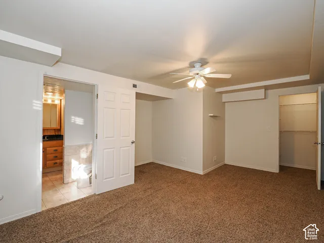 Interior space featuring neutral wall-to-wall carpeting, ceiling fan with integrated lighting, and walk-in closet with built-in shelving
