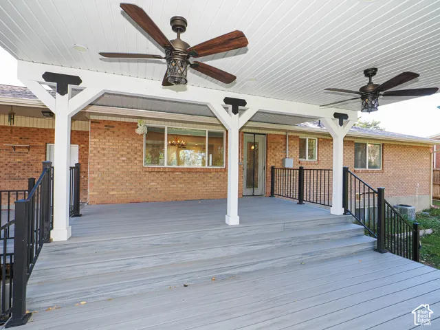 Covered deck featuring gray composite decking, two ceiling fans, white support columns with decorative corbels, and black metal railing