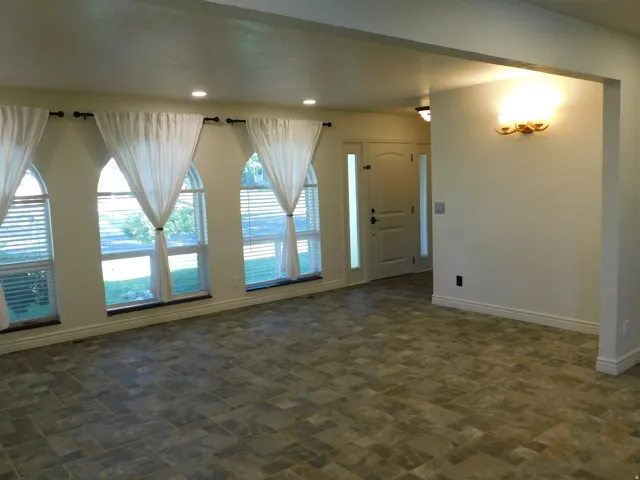 Arched windows with blinds, recessed ceiling lighting, wall-mounted sconce, entry door with sidelights, and tiled flooring