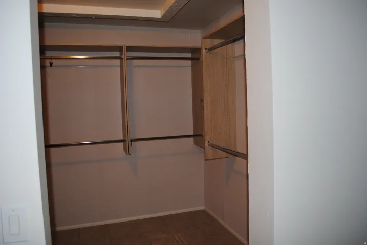 Walk-in closet with multiple hanging rods, integrated shelving, and tile flooring