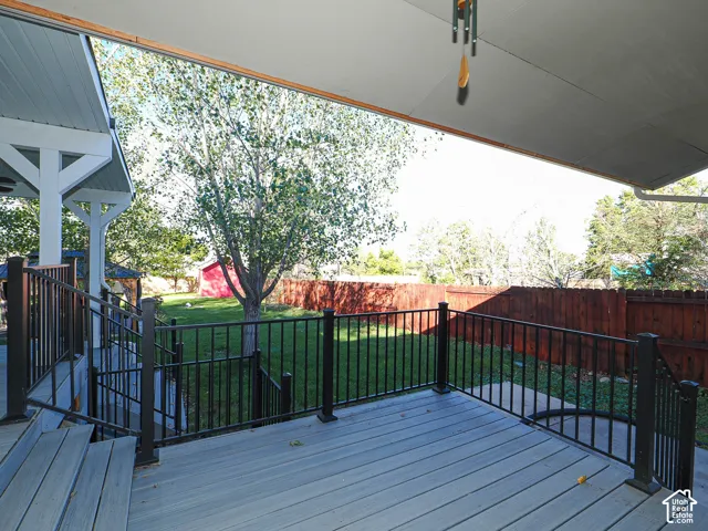 Covered outdoor deck featuring composite decking, black metal railings, and stairs leading to a fenced backyard