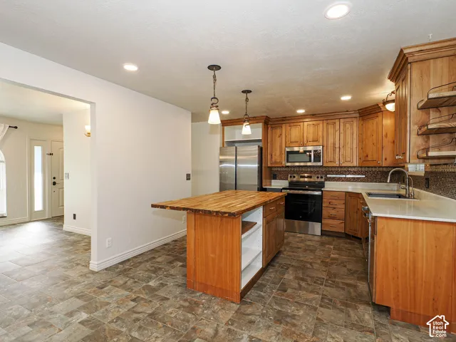 Kitchen featuring natural wood cabinetry, central island with a wood-block countertop, stone-tiled flooring, stainless steel appliances, and dual pendant lighting