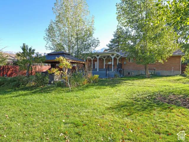 Expansive backyard featuring a covered gazebo, raised deck with decorative posts, brick exterior siding, and mature trees