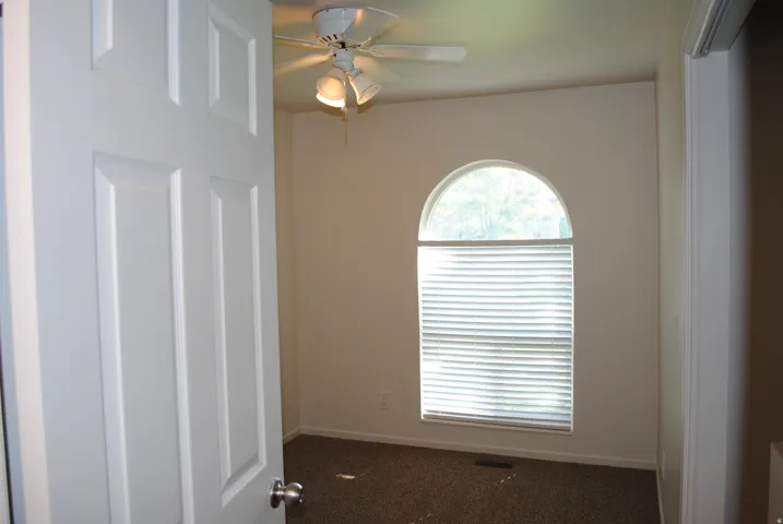 Arched window with blinds, ceiling fan with integrated lighting, paneled interior door, and textured carpeting