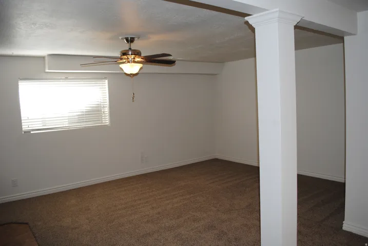 Carpeted interior with a single window, a ceiling fan with integrated lighting, and a structural column with decorative molding