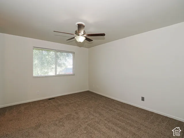 Interior space featuring neutral-toned carpeting, a sliding window with horizontal blinds, and a central ceiling fan with an integrated light fixture