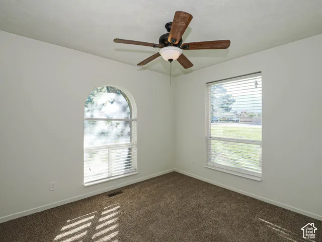 Neutral-toned room featuring a vaulted arched window, a secondary rectangular window, wall-to-wall carpeting, and a central ceiling fan with integrated lighting