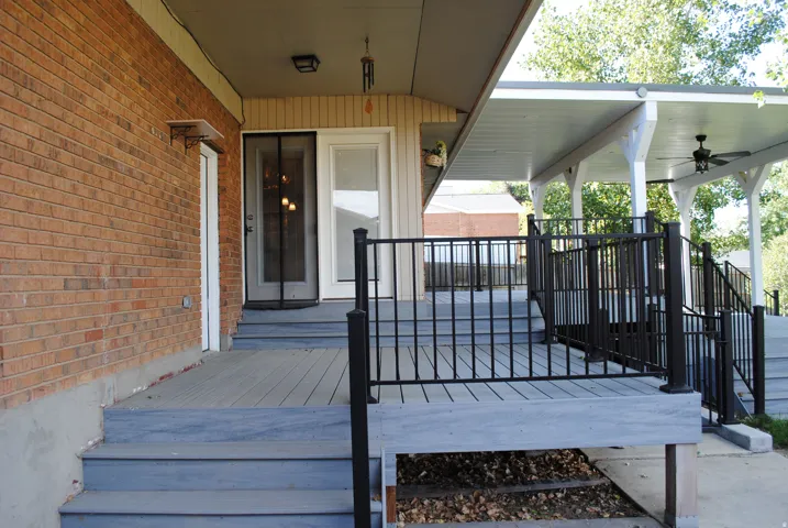 Brick exterior with a covered deck, featuring a ceiling fan and black railings