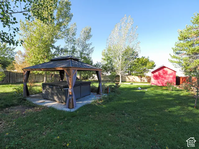 Expansive backyard featuring a covered outdoor structure with a metal roof, a concrete pad, a detached storage shed, and mature trees