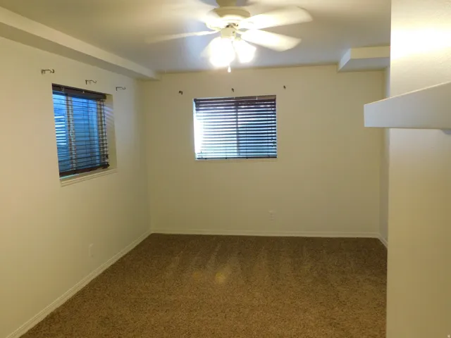 Carpeted flooring, two windows with blinds, ceiling fan, and built-in shelving