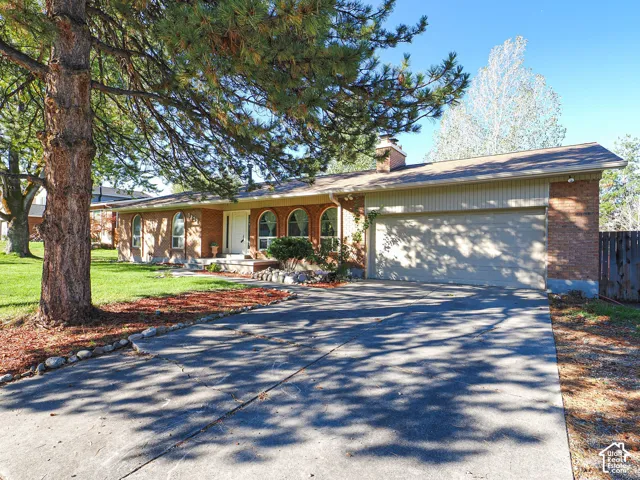 Single-story brick exterior featuring an arched window design, attached two-car garage, prominent stone-finish chimney, and mature landscaping
