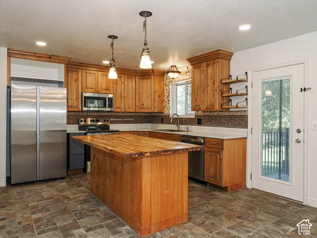 Kitchen featuring wood cabinetry, butcher block island countertop, stone-finish tile flooring, decorative tiled backsplash, and stainless steel appliances