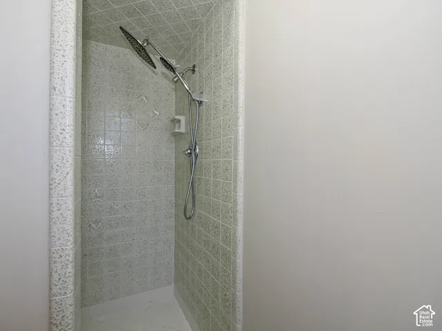 Walk-in shower enclosure featuring light-toned square tile surround, chrome rainfall showerhead, and integrated handheld shower fixture